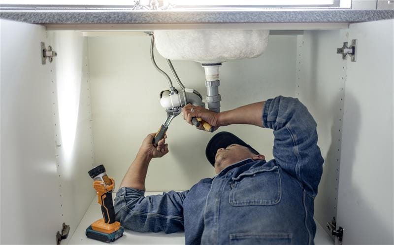 Plumber repairing pipes beneath a bathroom sink in Alpharetta