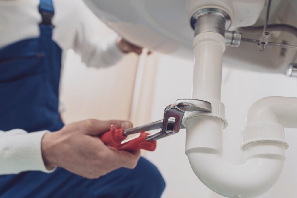 Plumber repairing a white drain pipe beneath a sink in Alpharetta