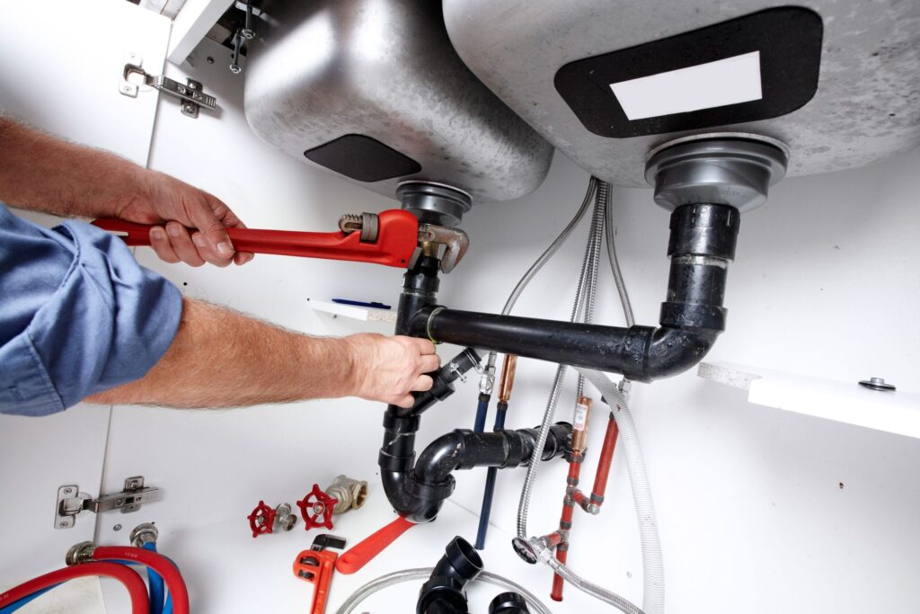 Plumber repairing drain pipes beneath a kitchen sink in Alpharetta
